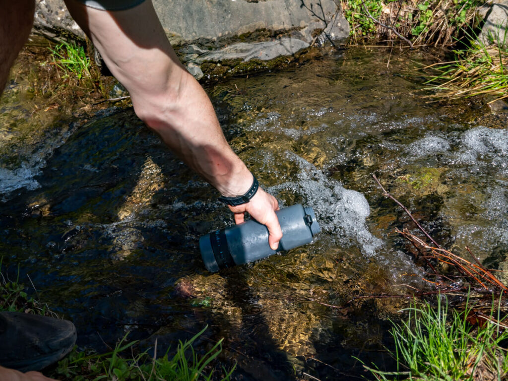 Dan's arm holding a filter water bottle in a stream on the Three Peaks trail in Prokletije National Park.