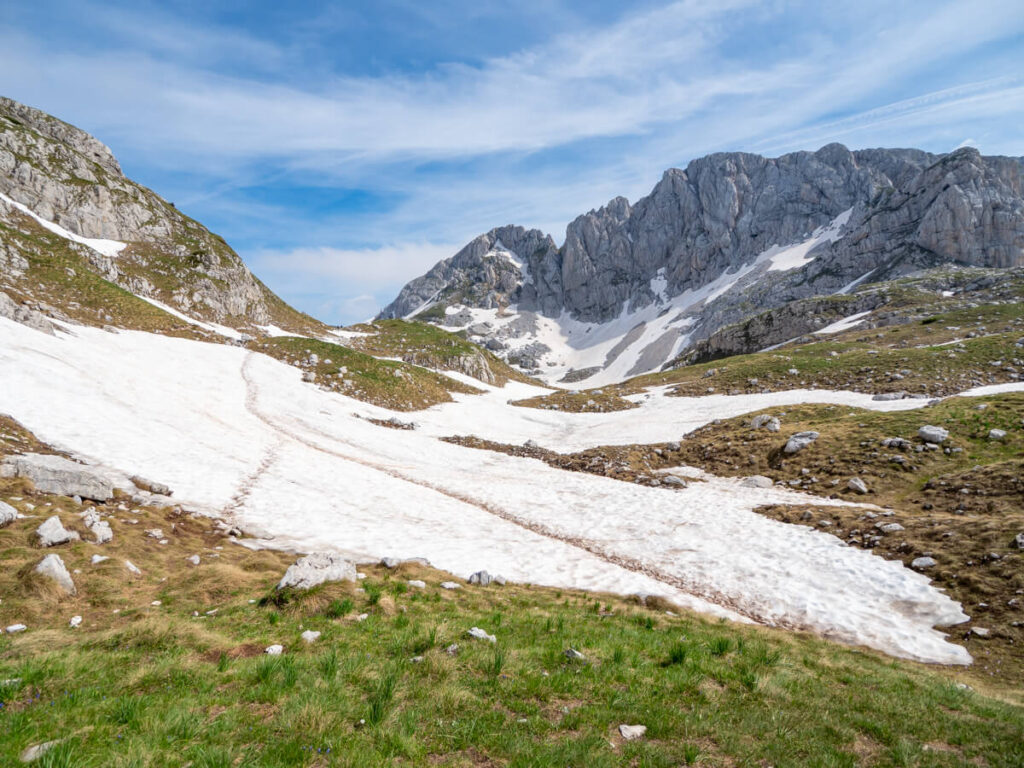 Multiple sets of footprints crossing a snowbank in a valley on the Bobotov Kuk trail.