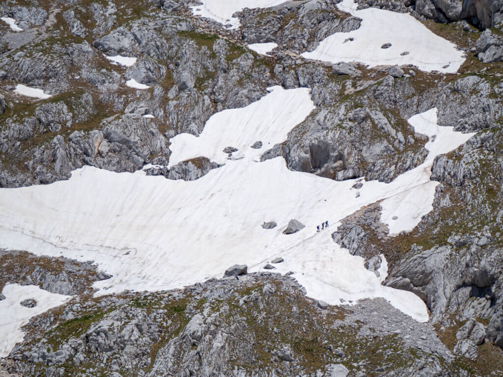 Three hikers in the distance climbing the steep and snowy side of Bobotov Kuk.