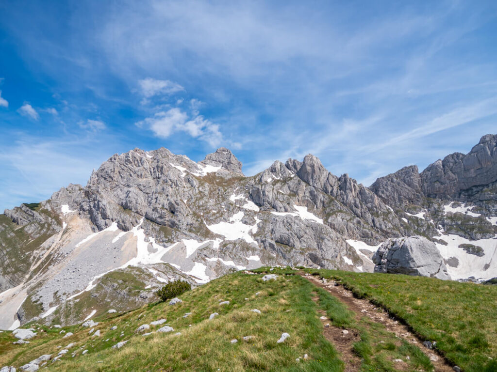 A dirt trail leading towards a grassy ridgeline before the snowy Bobotov Kuk.