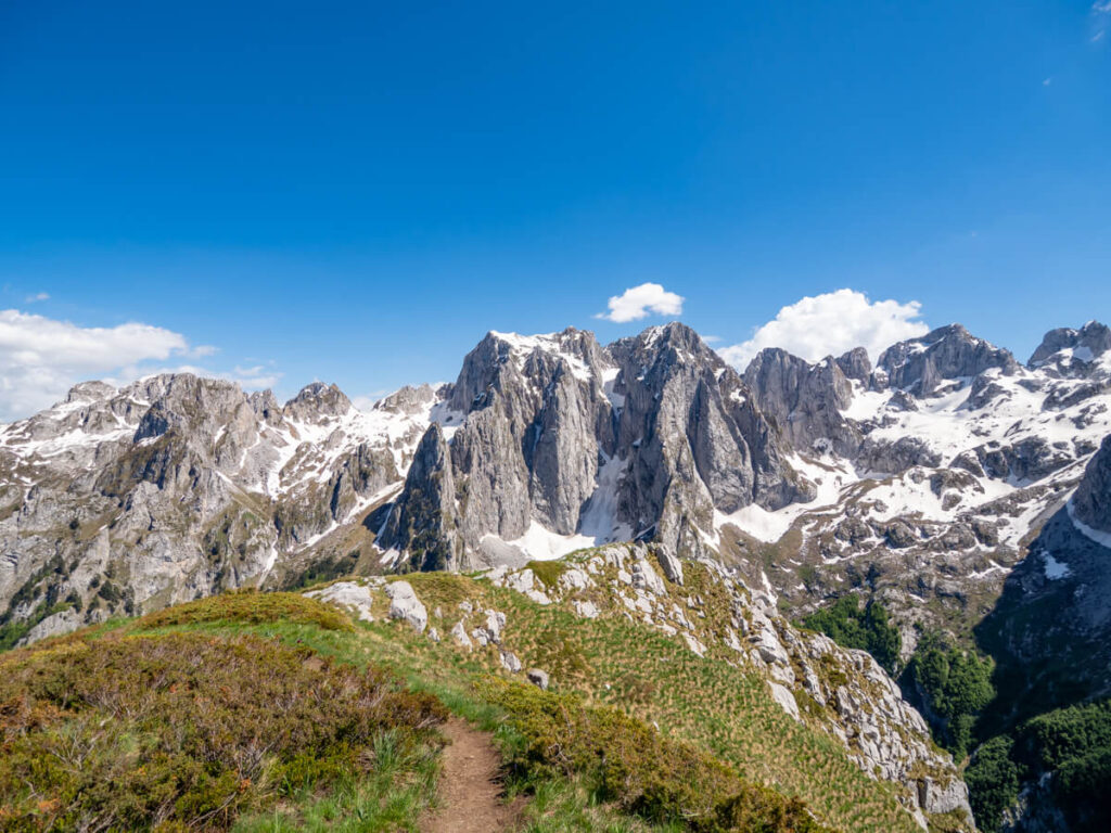 A dirt trail leading to a viewpoint of the tall Karanfili mountains topped with snow on the Three Peaks trail in Prokletije National Park.