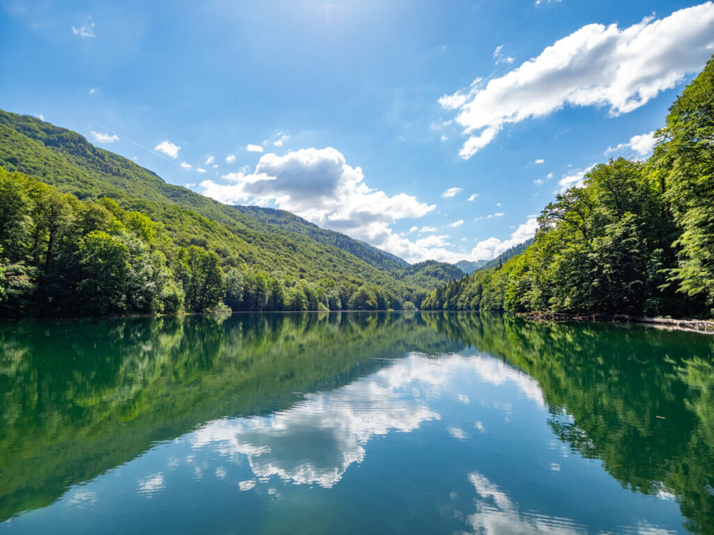 Clouds reflected in the still surface of Lake Biograd, lined with trees.