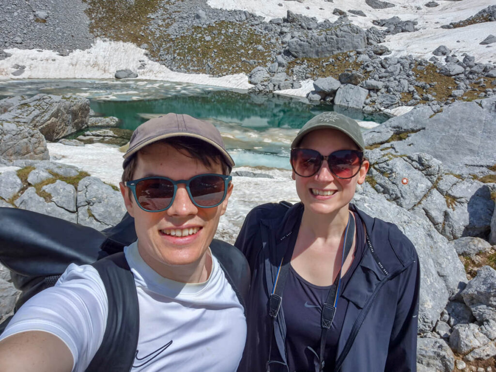 Lucy and Dan smiling in front of the Zeleni Vir glacial lake surrounded by rocks and snow.