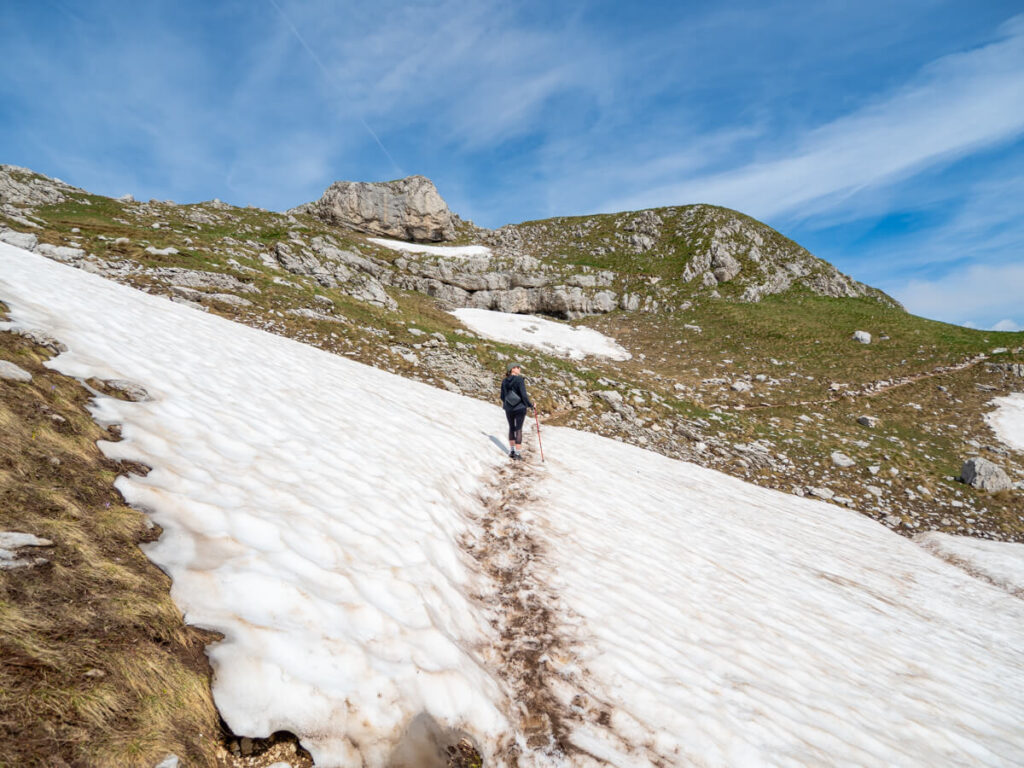 Lucy holding trekking poles and hiking across a snowbank on the Bobotov Kuk trail.