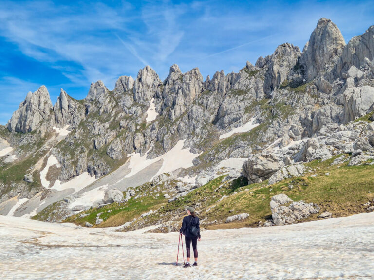 Lucy holding hiking poles on an expansive ice field looking at jagged limestone peaks on the Bobotov Kuk hike in Durmitor National Park.