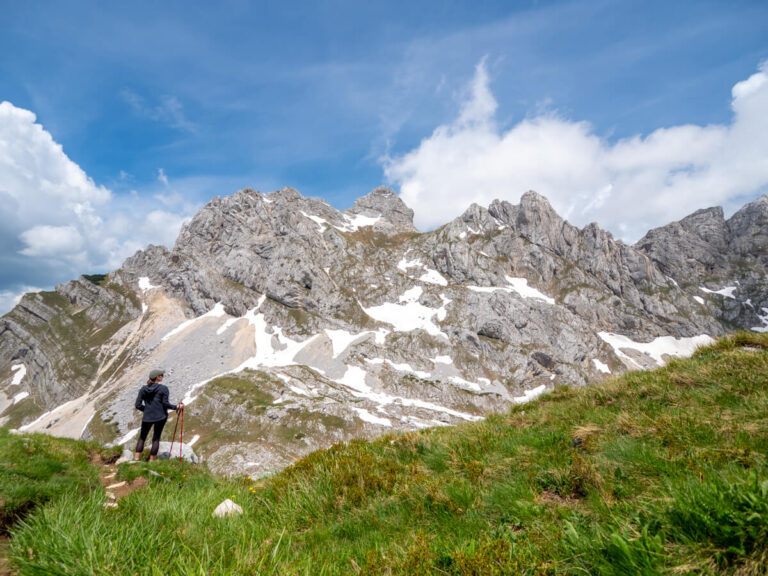 Lucy holding trekking poles while looking at Bobotov Kuk peak from a grassy ridge on the trail.