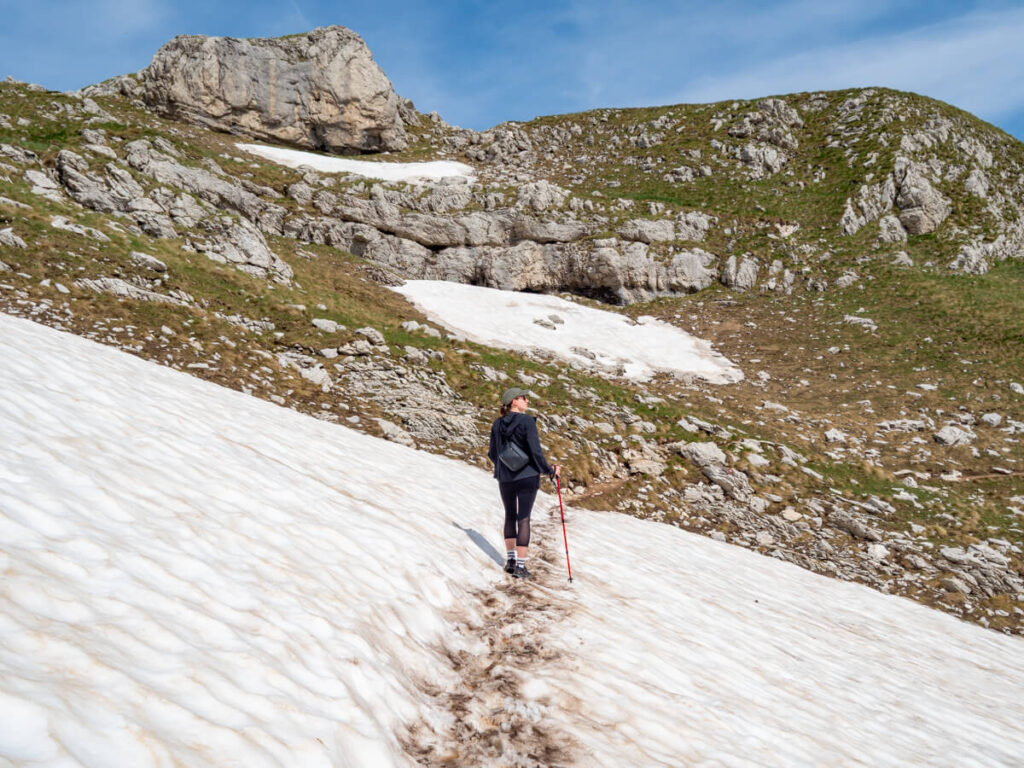 Lucy hiking on an ice field with trekking poles on the Bobotov Kuk trail in Durmitor National Park.