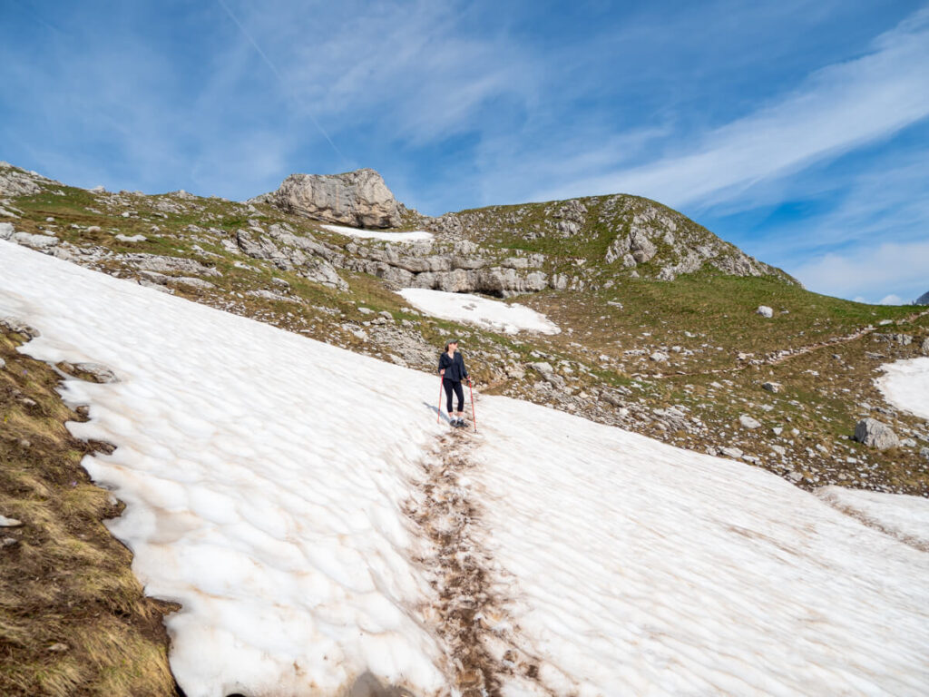Lucy standing on a snowfield looking out at the mountians of Durmitor National Park on the Bobotov Kuk Trail.