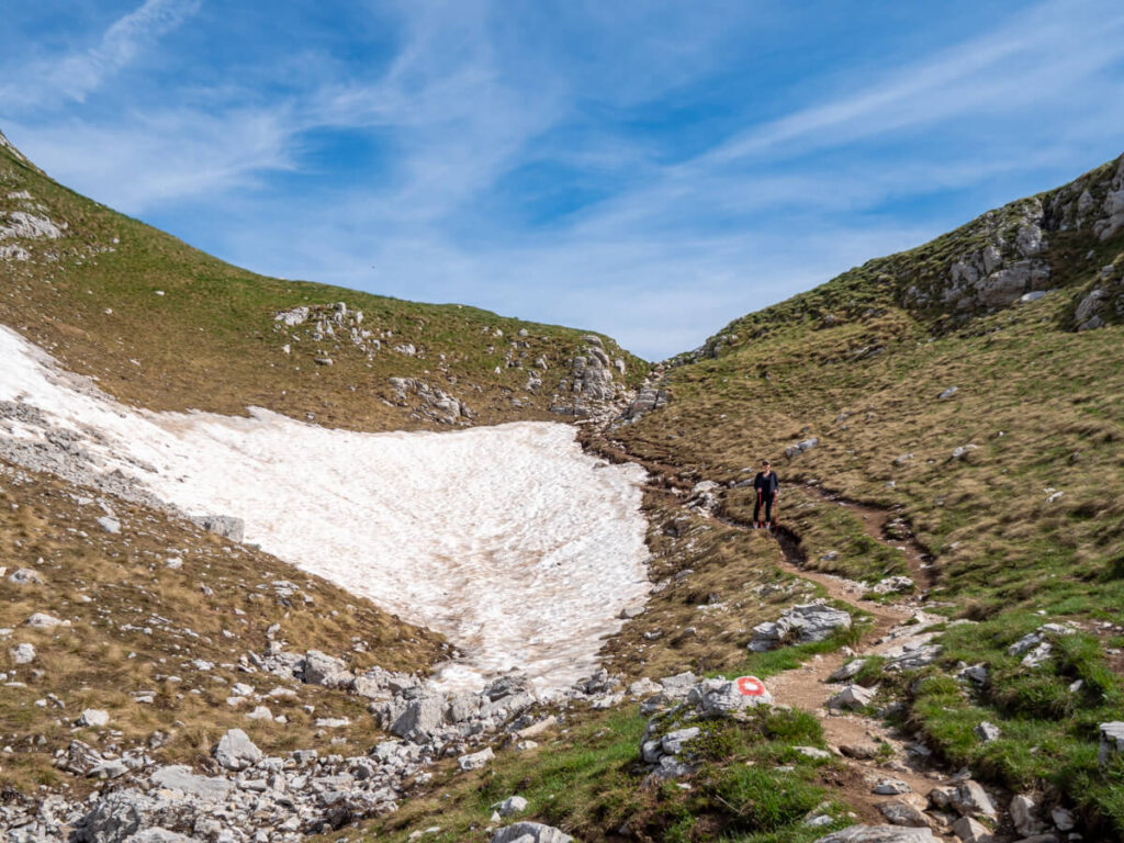 Lucy standing by a vast snowbank in a valley on the Bobotov Kuk trail.