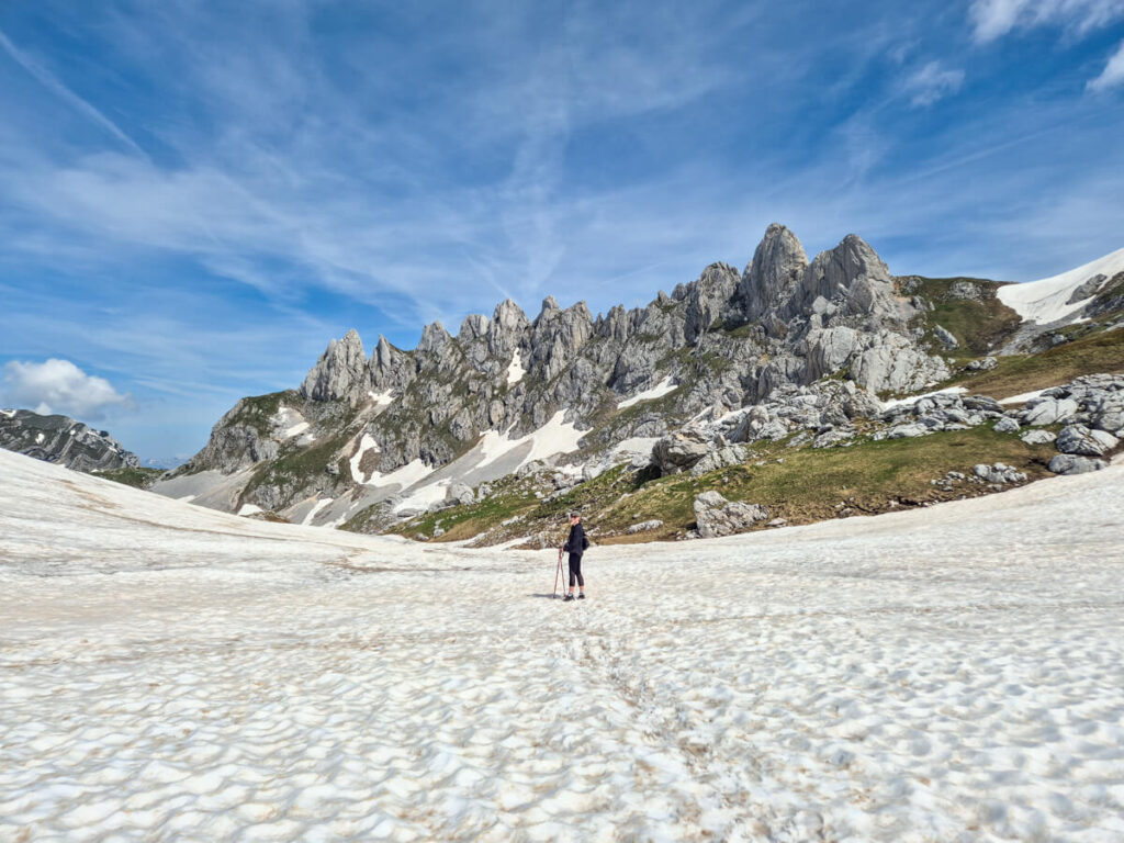 Lucy walking across snow towards the impressive jagged Zupci mountain peaks on the Bobotov Kuk trail.