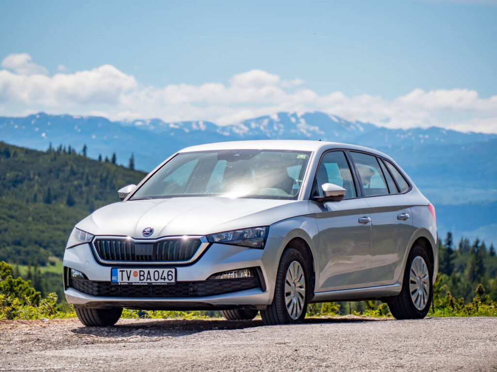 A silver Skoda from Kombo Rent a Car, backed by snowy mountains in Durmitor National Park.