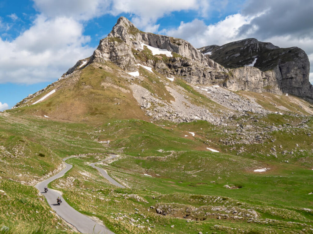 Two motorbikes driving down a winding road in a valley below Sedlena Greda in Durmitor National Park.