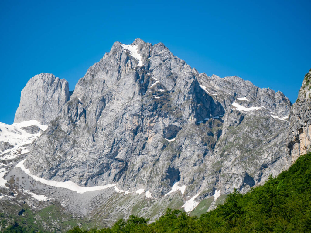 Jagged limestone cliffs with a tiny bit of snow on top and green forest below in the Grebaje Valley.