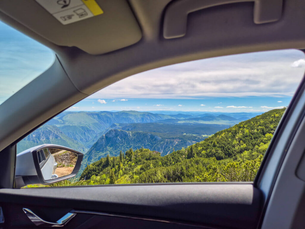 The view from the passenger's side window of a car showing the impressive mountains, valleys, and forests in Durmitor National Park.