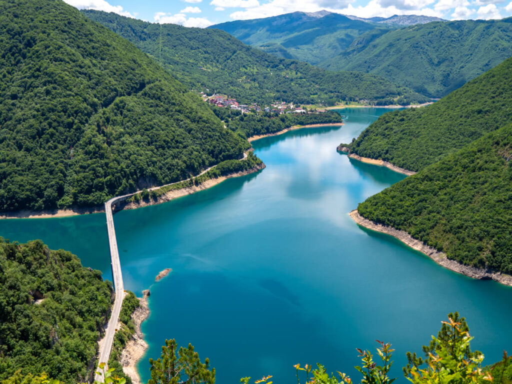 The calm, blue waters of Piva Lake dominated by green canyon walls, viewed from a high viewpoint.