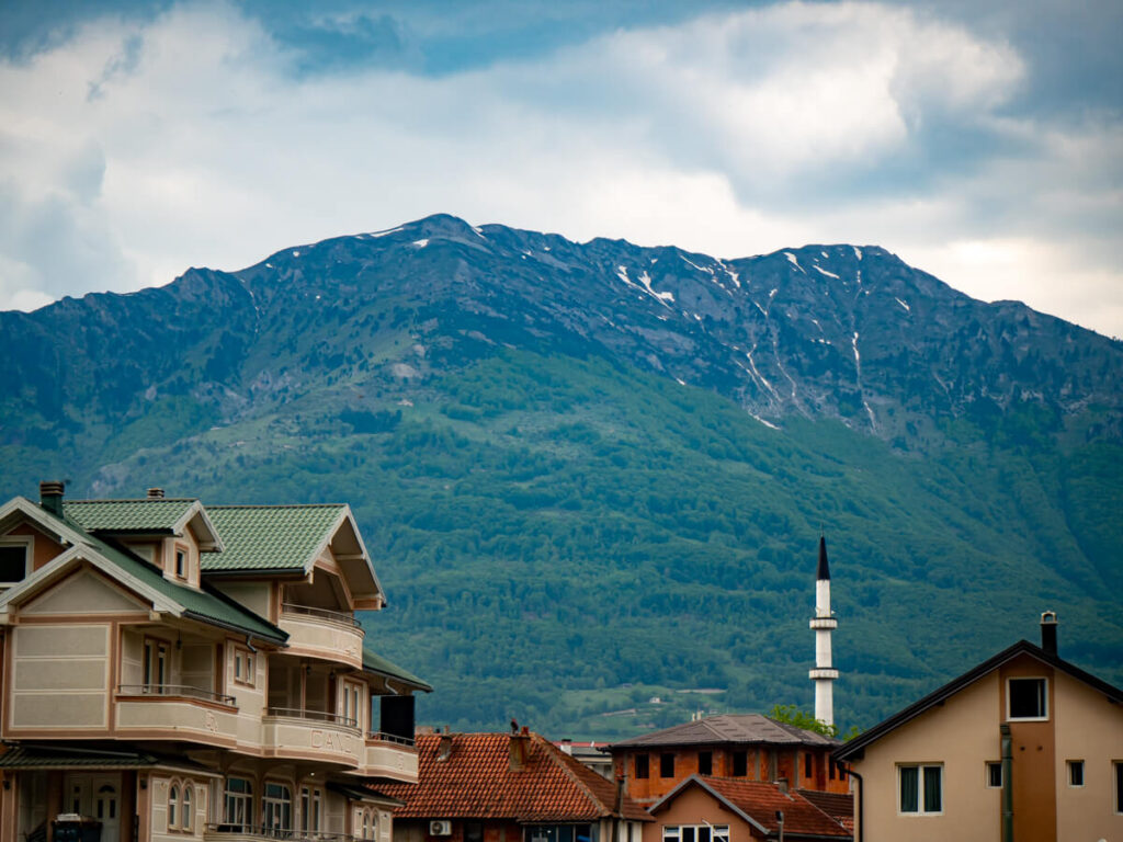 A mosque minaret against a green mountain in Plav, Montenegro.