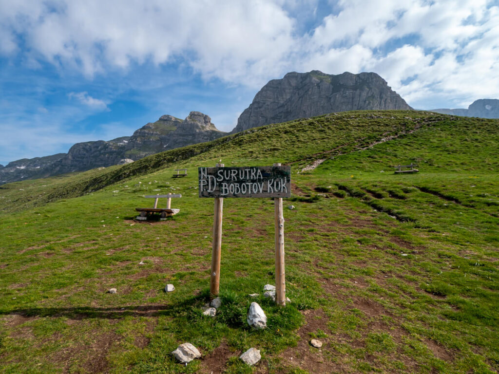 A green wooden sign indicating the start of the Bobotov Kuk trail in Sedlo Pass.