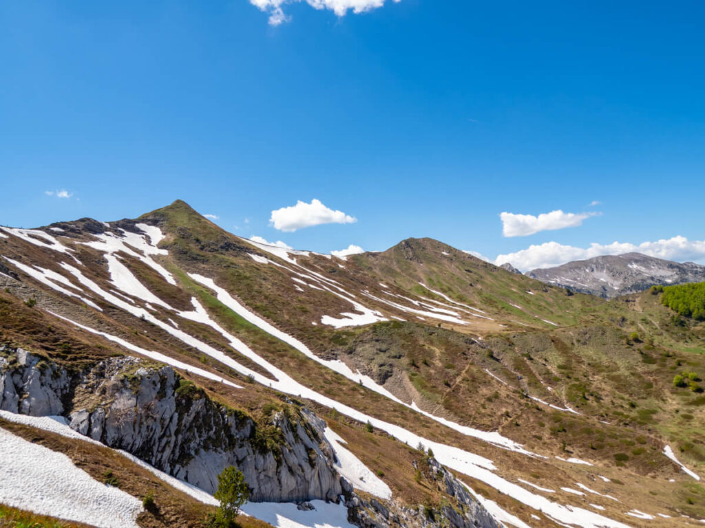 A wide valley backed by the peaks of Popadija and Talijanka and strewn with snow on the Three Peaks hike in Prokletije National Park.