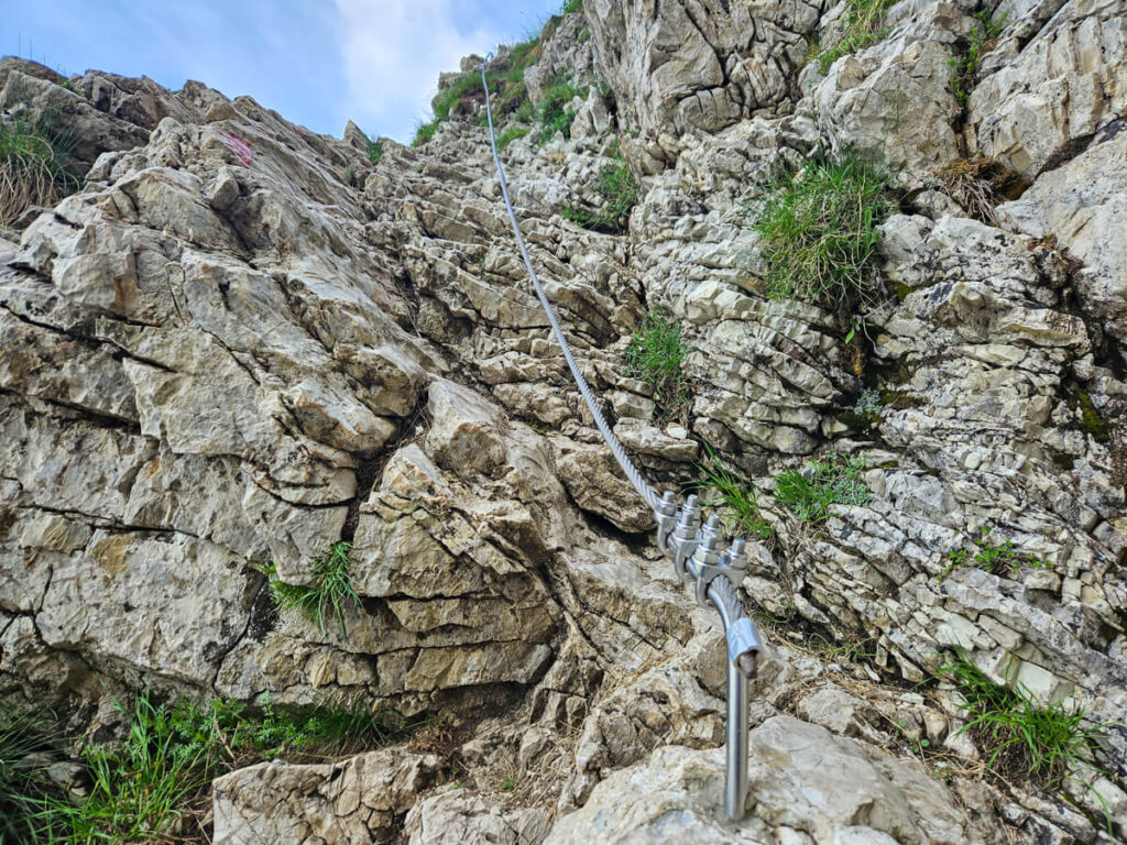 A steel cable attached to the rockface on the Snow covering a narrow scree-covered trail on the Bobotov Kuk hiking trail.