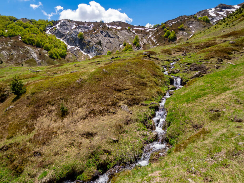 A stream trickling through a green meadow on the Three Peaks trail in Prokletije National Park.