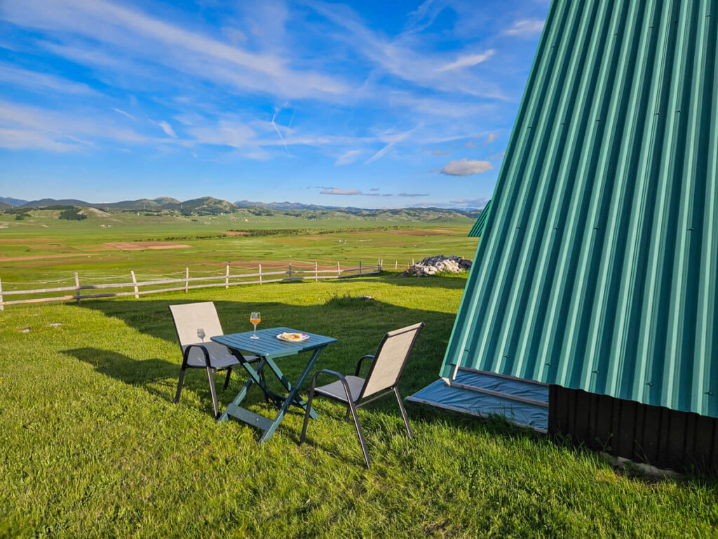 A table and chairs in the sunshine beside the green roof of an A-frame cabin in Durmitor National Park.