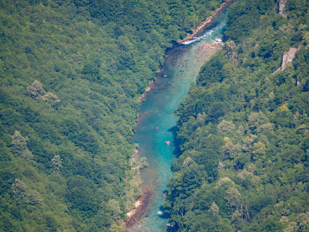 Tiny red white water river rafts floating down the turquoise Tara River in Durmitor National Park, viewed from above.