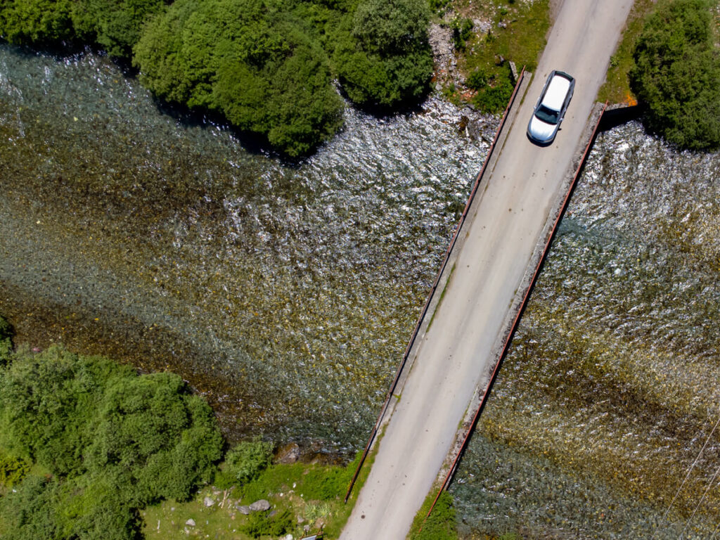 An aerial view of a hire car driving over a small bridge in Prokletije National Park, Montenegro.