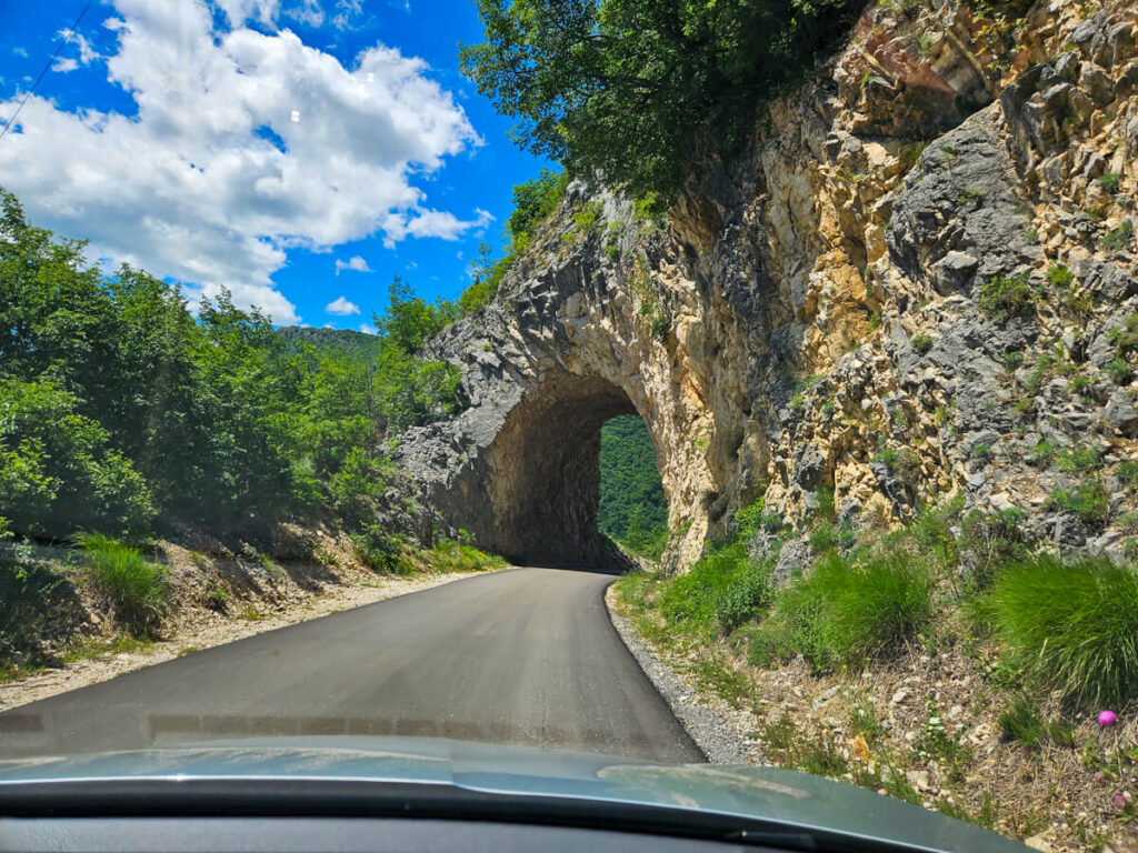 A road leading to a small tunnel carved out of the mountainside close to Piva Lake and Durmitor National Park. The photo has been taken from the driver's point-of-view.