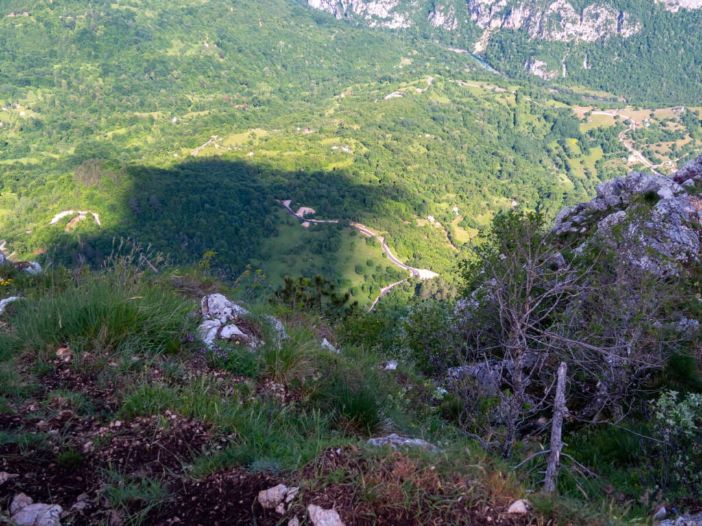 A winding road in the distance at teh bottom of a valley, viewed from the Ćurevac Trail.