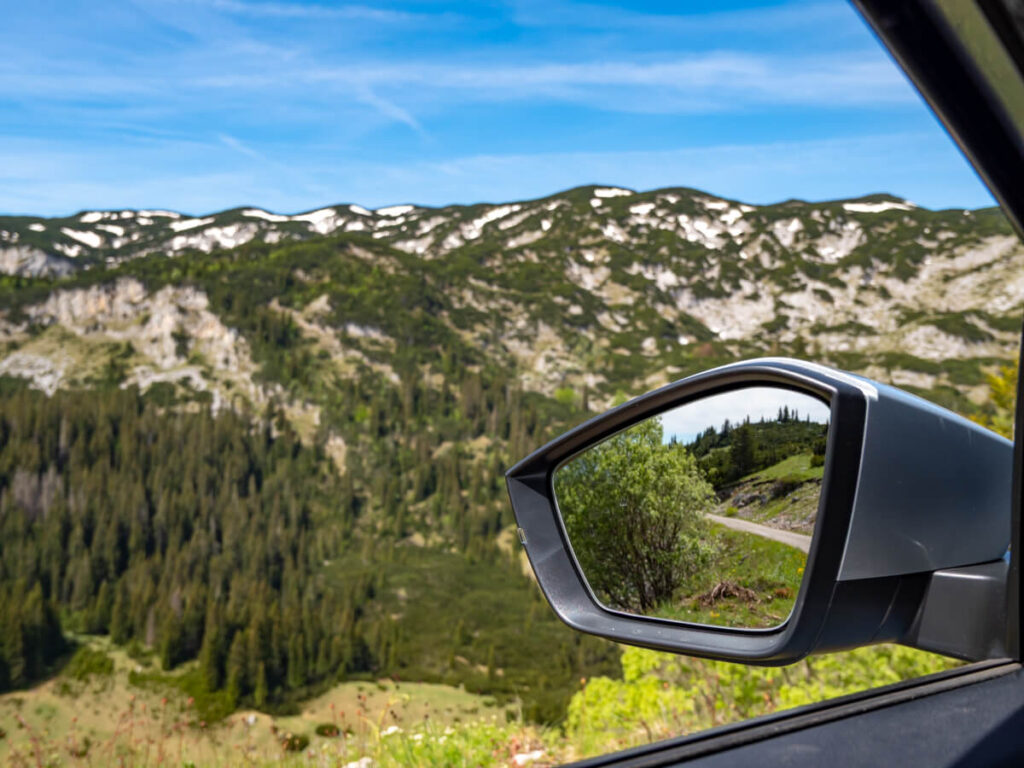 The view from a car window of forests and hills, as well as the view of more greenery seen reflected in car's the wing mirror, in Durmitor National Park.