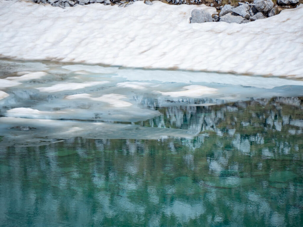 The icy blue water of Zeleni Vir lined with snow at the foot of Bobotov Kuk.