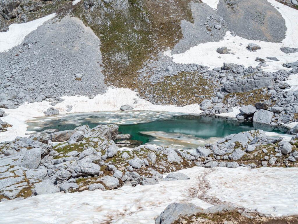 A circular icy blue lake surrounded by snow in a valley on the Bobotov Kuk hike.