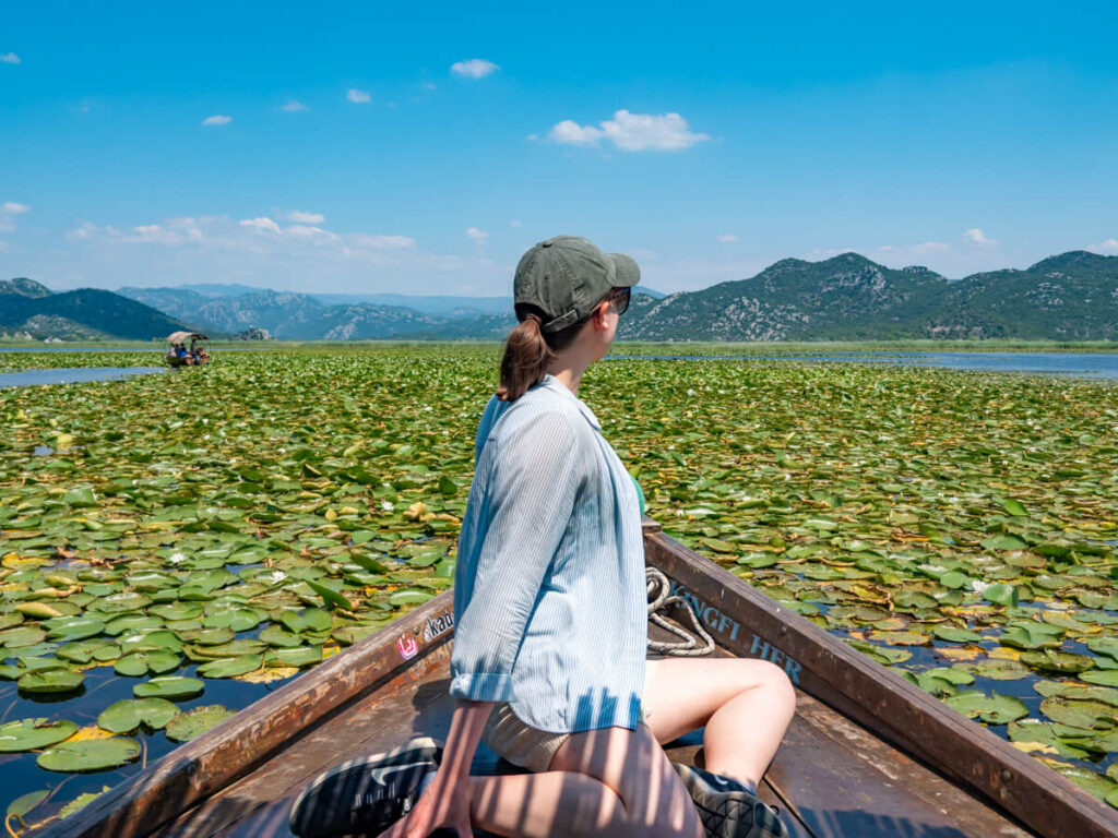 Lucy on the front of a wooden boat surrounded by lily pads on a Lake Skadar tour.