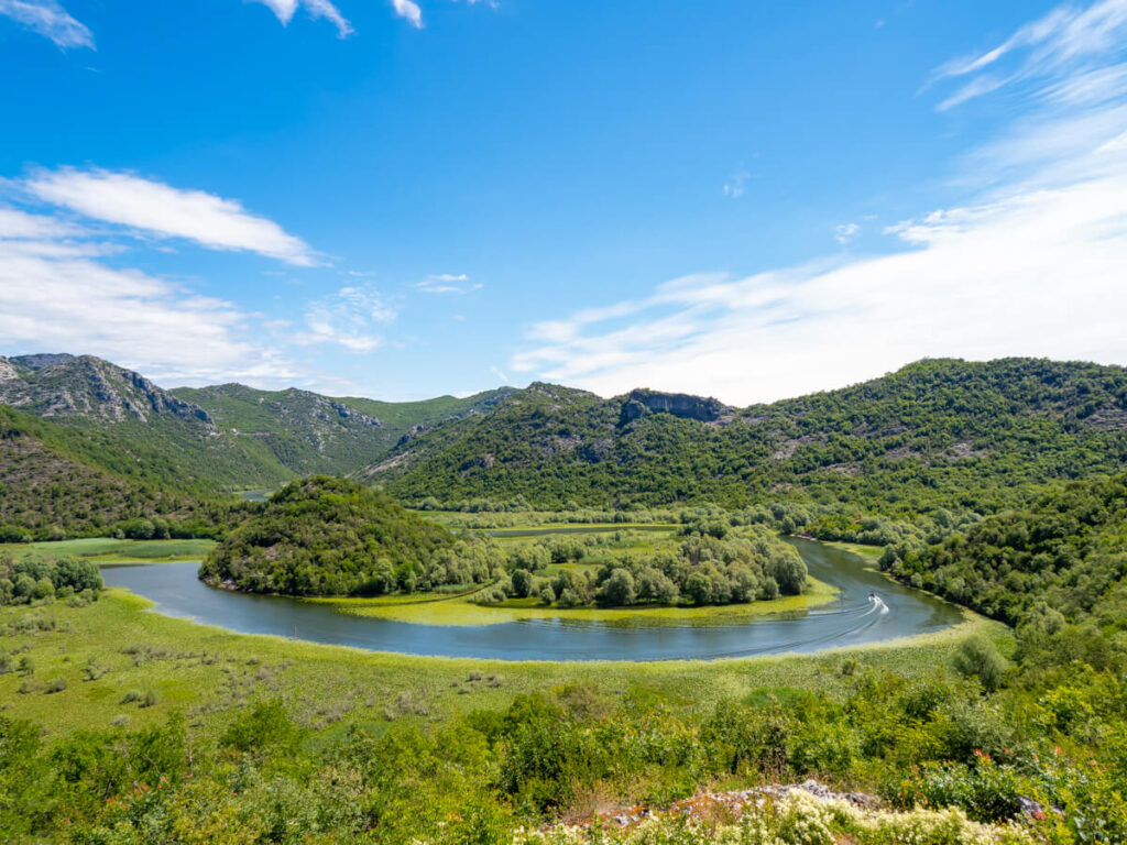 A blue riverbend winding around lush green mountains near Lake Skadar.