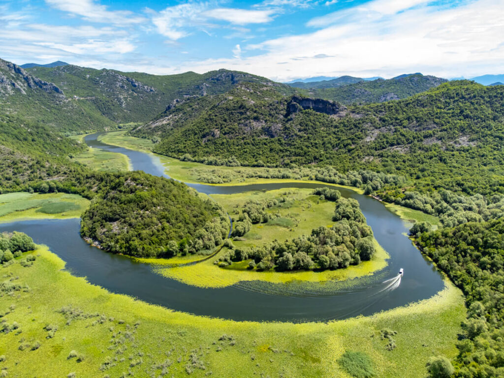 A boat travelling around a horseshoe riverbend near Rijeka Crnojevića and Lake Skadar as viewed from a drone.