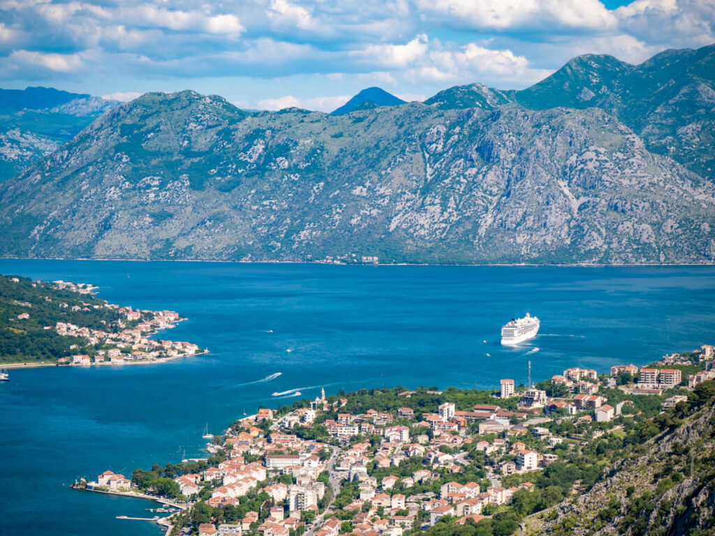 A cruise ship docked in the middle of the blue Bay of Kotor, lined with houses.