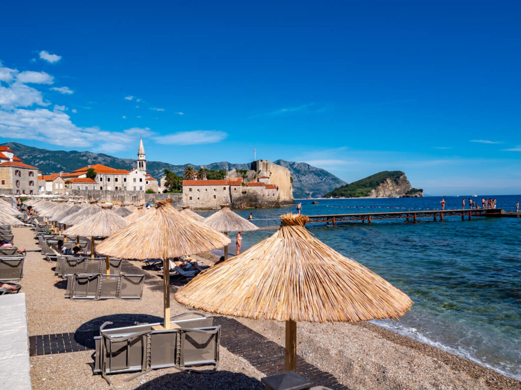 Sun loungers and thatched umbrellas on a beach in Budva near the Old Town.