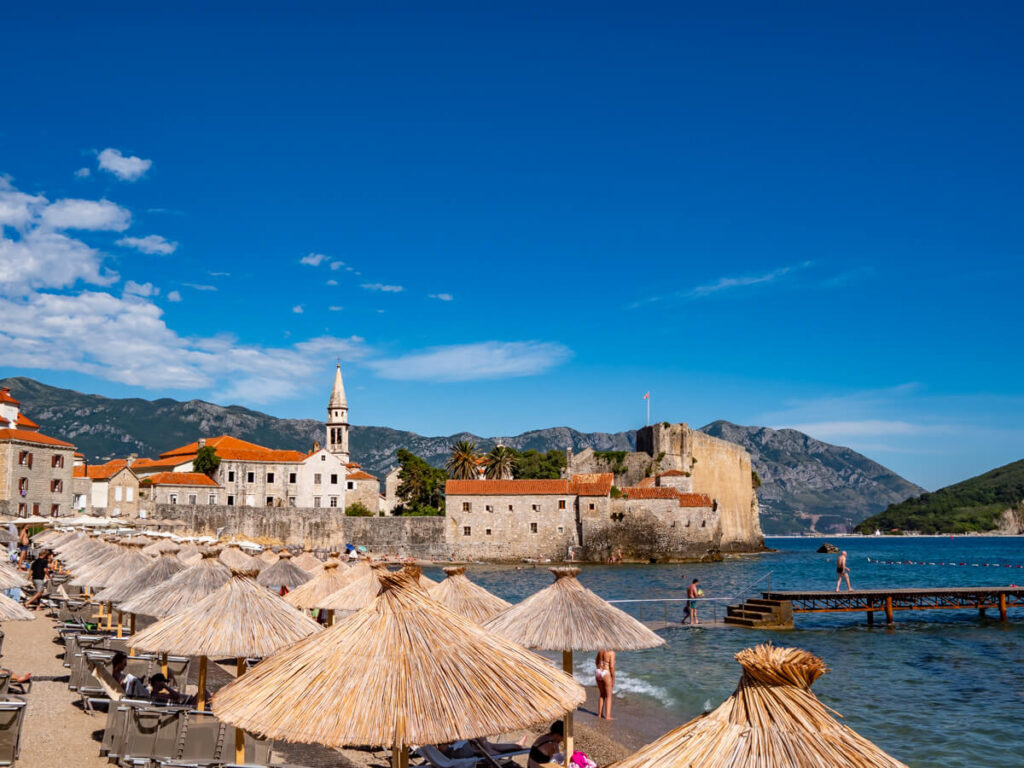 Thatched umbrellas on a beach by Budva's Old Town.