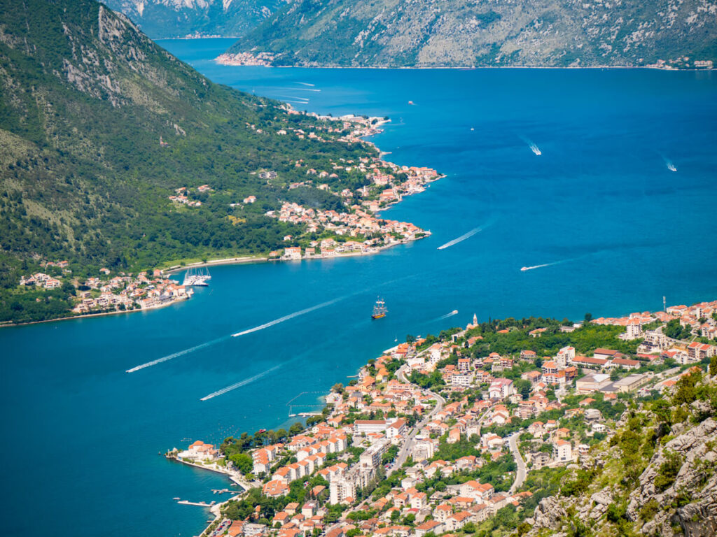Boats cruising around the Bay of Kotor, surrounded by luscious green mountains and old coastal towns.