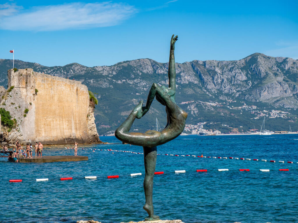 The faded bronze Budva Ballerina statue in front of the Adriatic Sea.