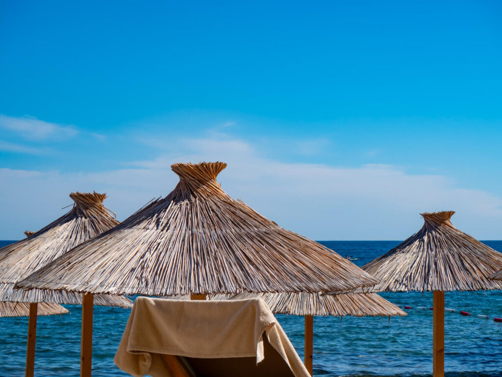 Thatched umbrellas and a towel on a sun lounger on a beach in Budva, Montenegro.