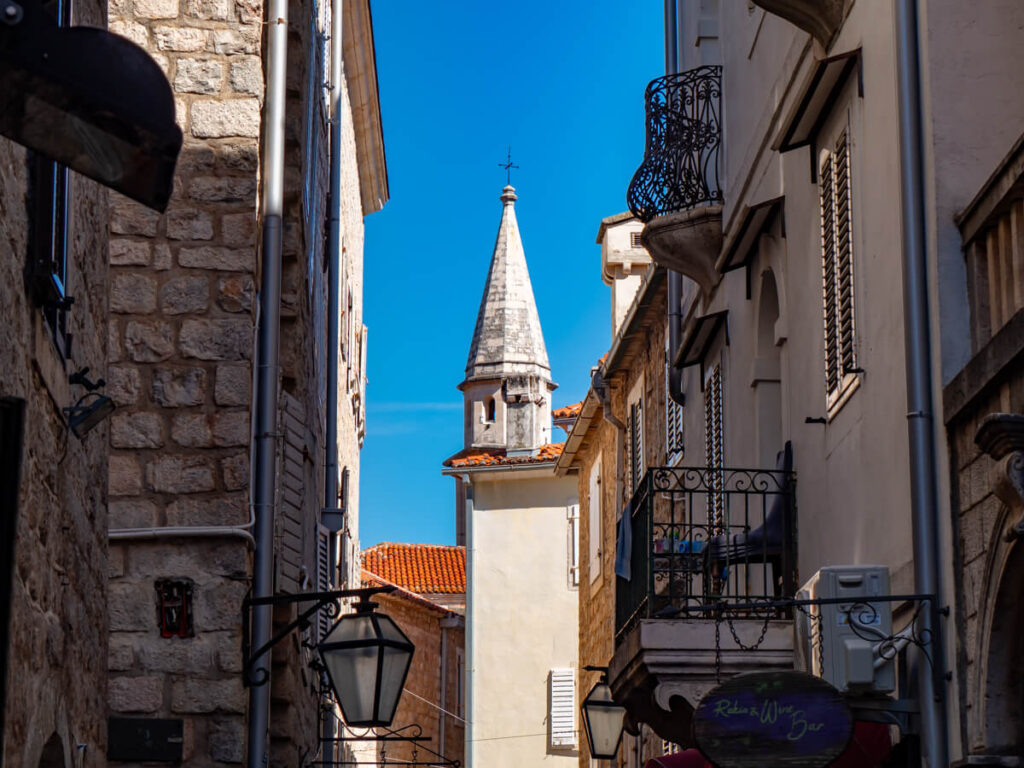 A church tower framed by the buildings of Budva Old Town.