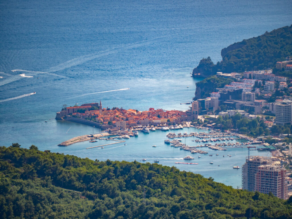 The red rooves of Budva Old Town encircled by a wall next to the more modern town, viewed from the main road uphill.