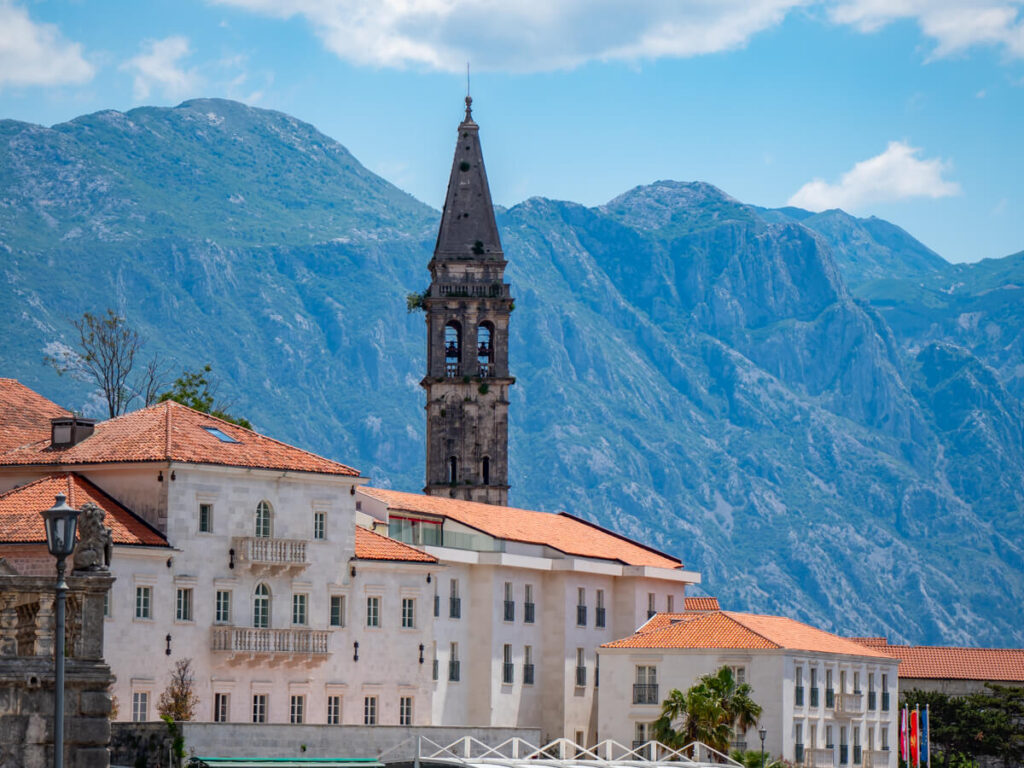 A church tower above red rooves set against the mountains of the Bay of Kotor.