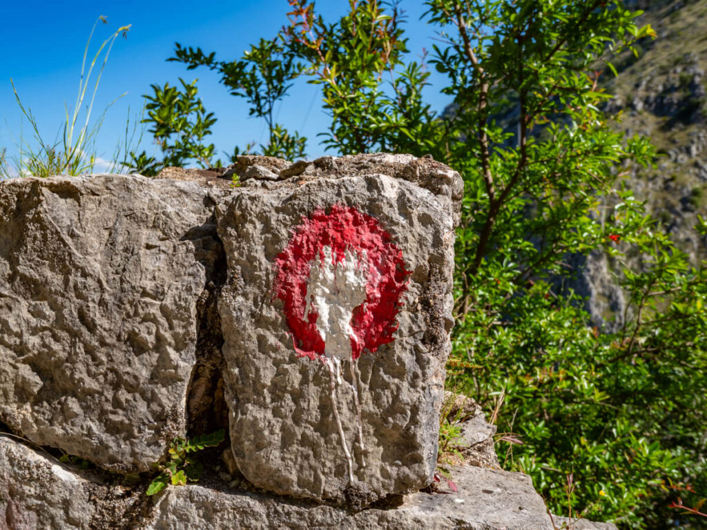 A circular red and white trail marker painted on a stone on the Ladder of Kotor trail.