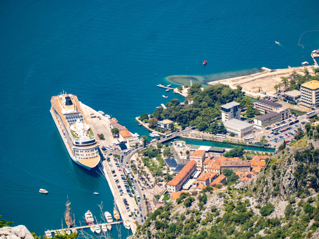 A cruise ship docked at the port in Kotor, viewed from above at a viewpoint on the road to Lovćen National Park.