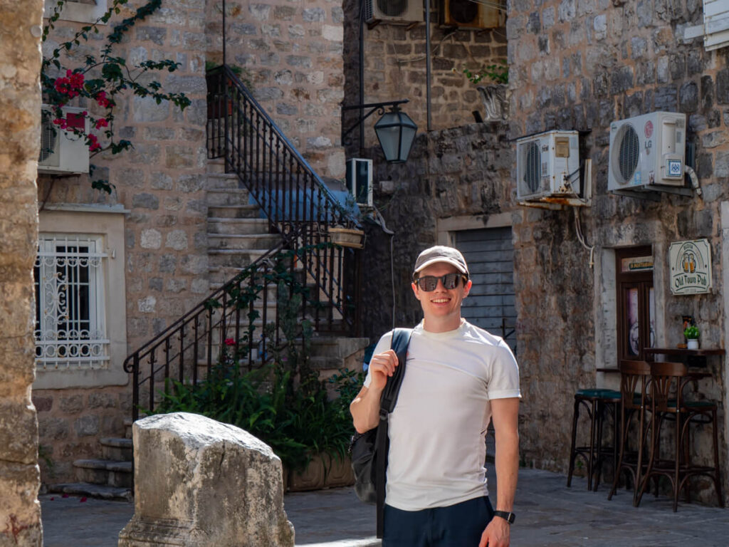 Dan standing in a square in Budva Old Town surrounded by stone buildings.
