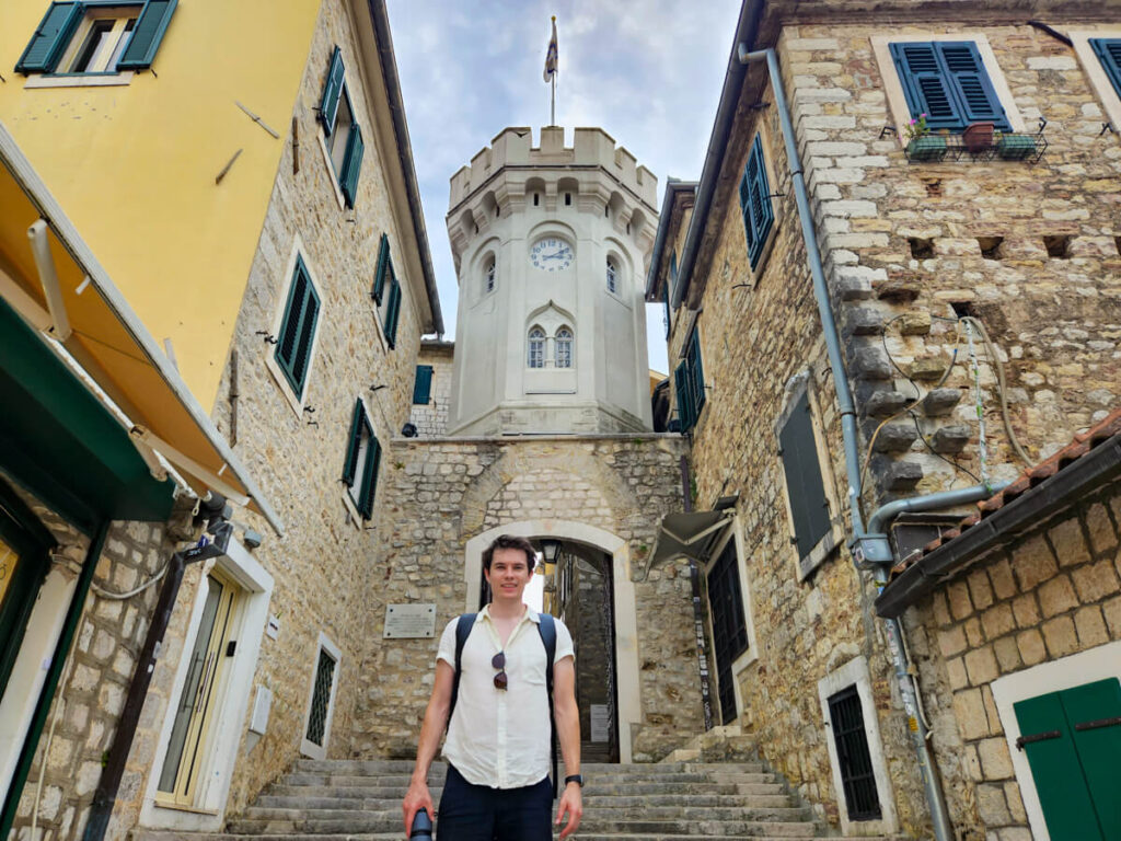 Dan standing in front of a clock tower on the cobbled streets of Herceg Novi, Montenegro.