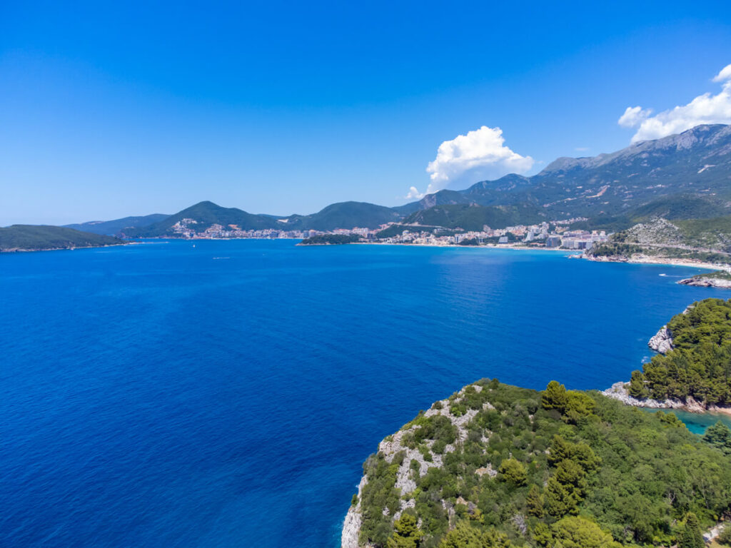A drone shot of Budva spread along Montenegro's coastline and the blue Adriatic Sea.