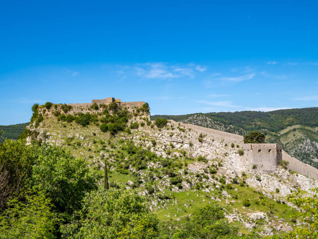 The walls of San Giovanni Fortress in Kotor on a green hilltop.